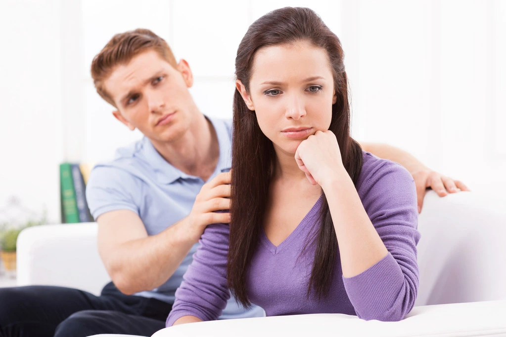 Leave me alone! Young man trying to comfort his depressed girlfriend sitting close to him on the couch