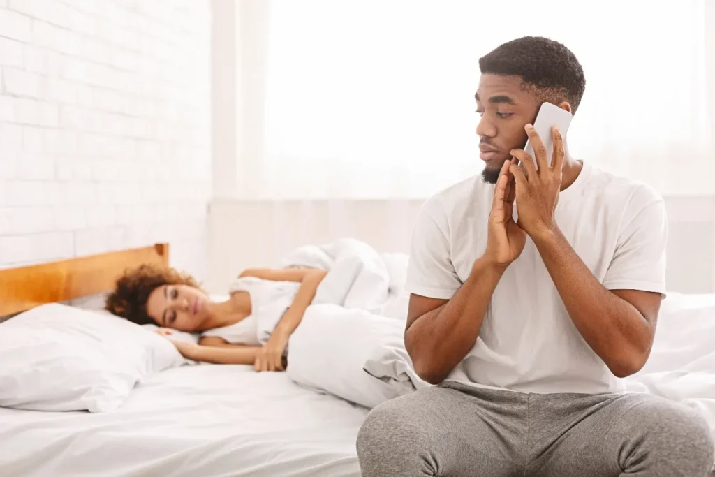 A man making a phone call while the girlfriend is sleeping